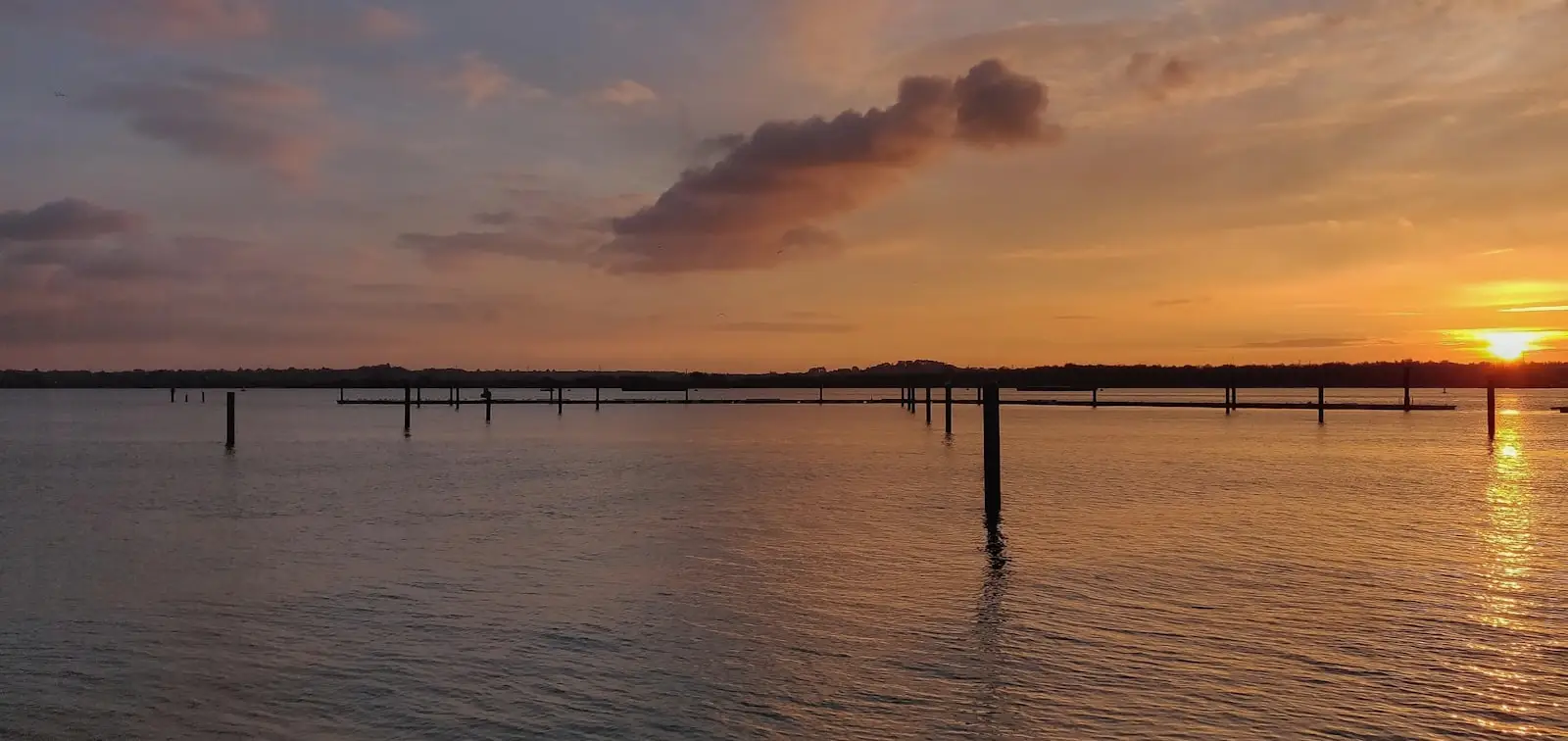 The Solent at dusk, with mooring posts reflected in calm water